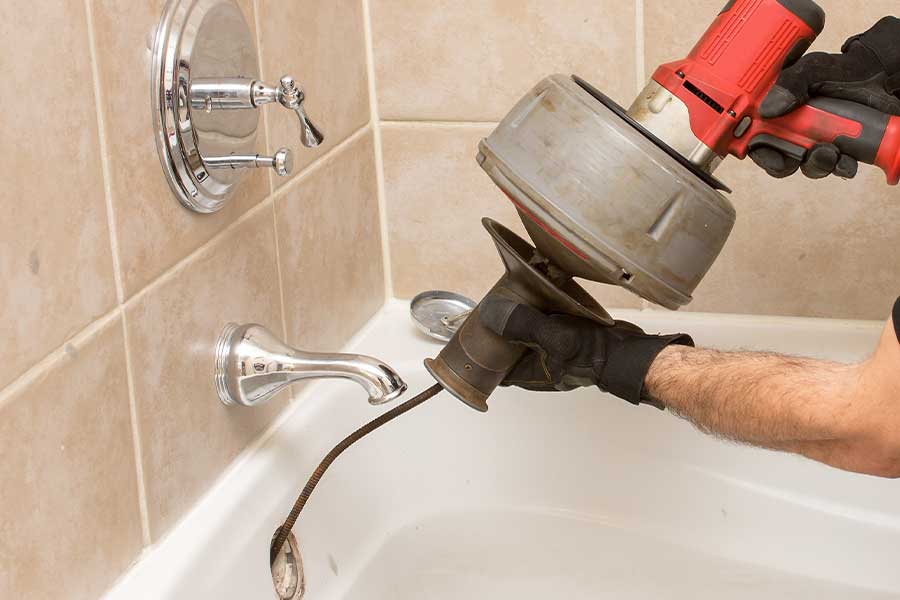 Plumber using drain snake to clear bathtub clog